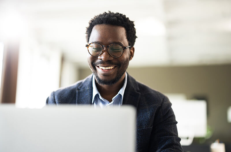 Happy businessman smiling while working on a laptop in a modern office, focused on productivity and success.