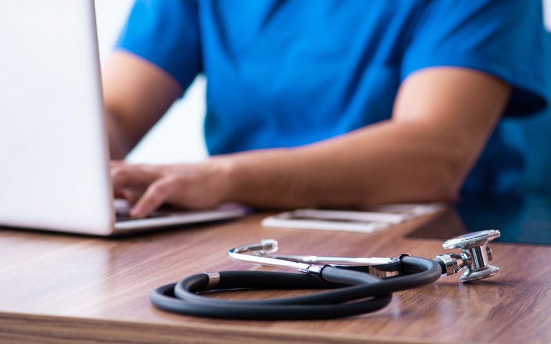 Nurse working on laptop computer with stethoscope nearby