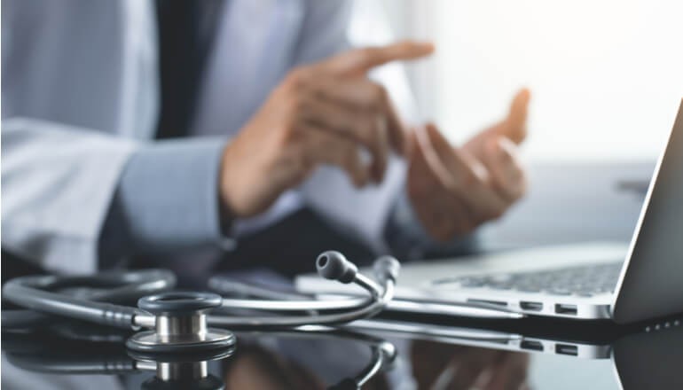 Close up of doctor using mobile device over laptop