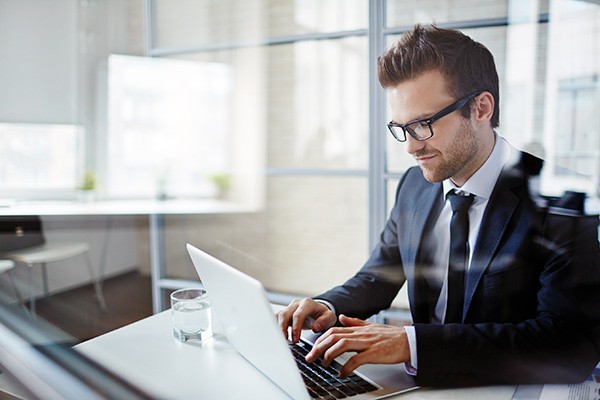 Smiling businessman in glasses works on computer