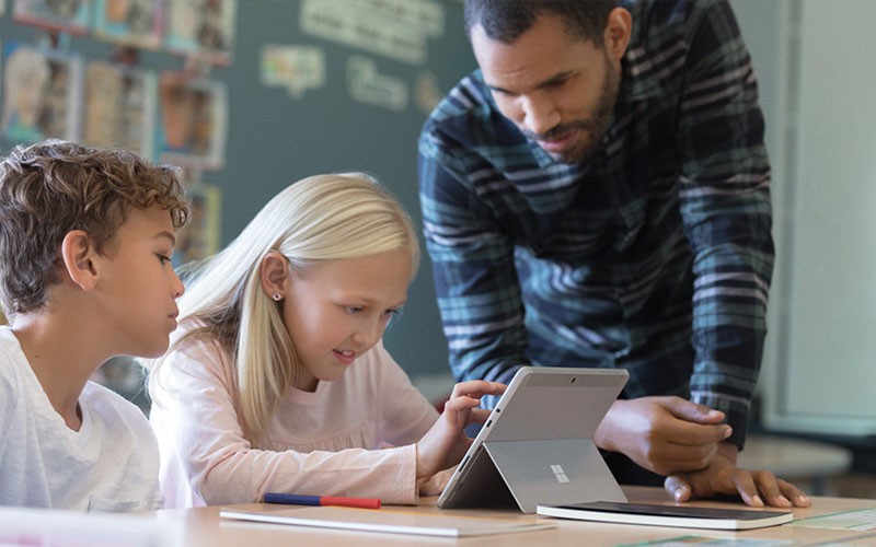 Immersive and modern learning tools Teacher uses Surface device to teach two students in classroom