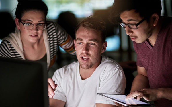 Group of IT professionals gathered around computer reading security reports