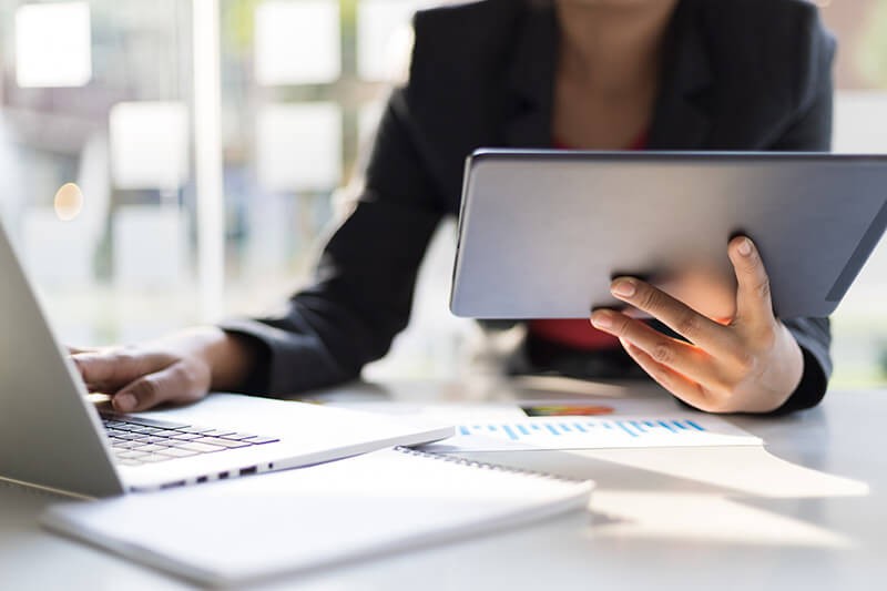 Businesswoman using tablet device while on laptop computer