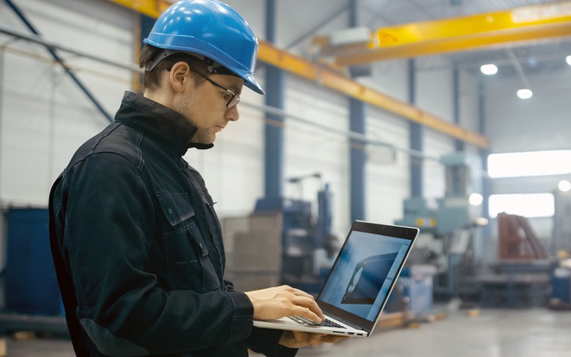 Man in hardhat on laptop in factory 