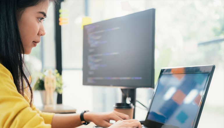 Businesswoman on laptop computer with code open on desktop