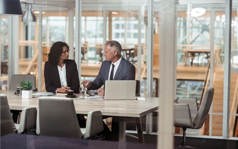 Two coworkers in office meeting room discussing over laptop device