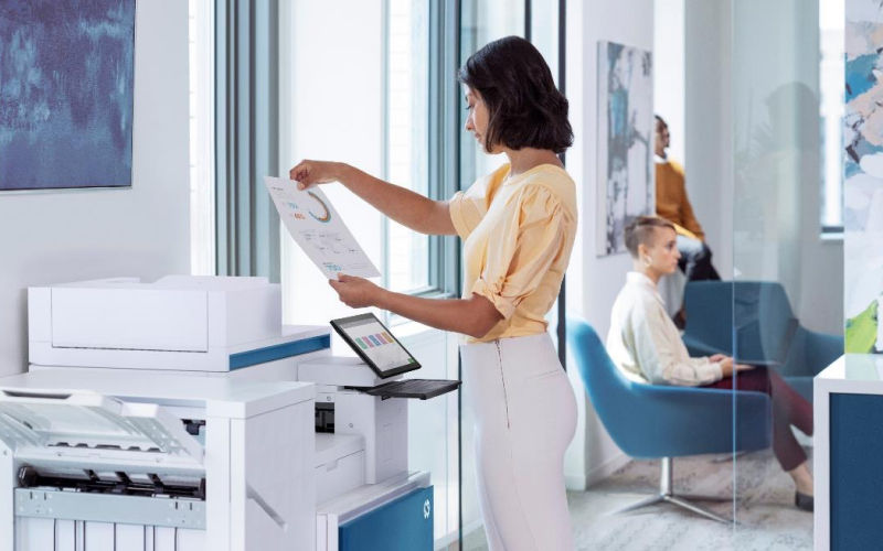 woman standing at hp printer looking at freshly printed papers