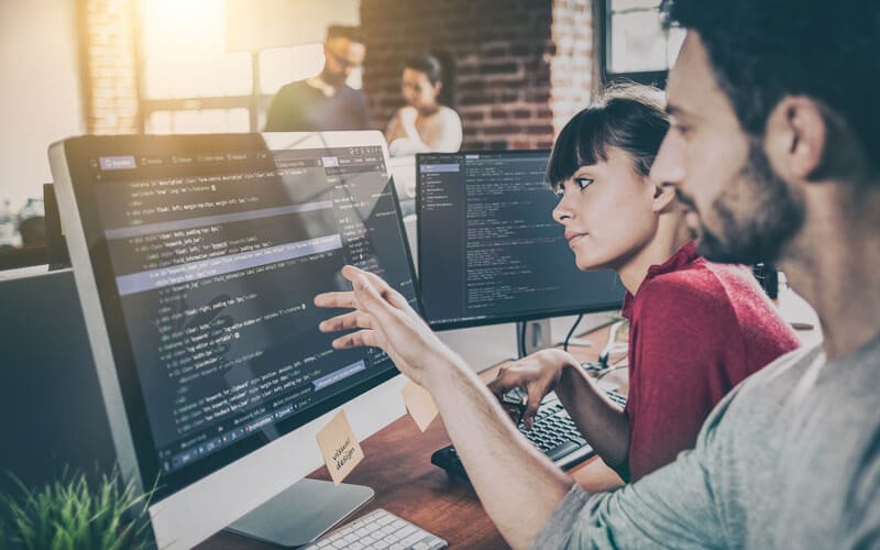 JBoss can help accelerate productivity and improve quality Two developers review code and data on desktop computers
