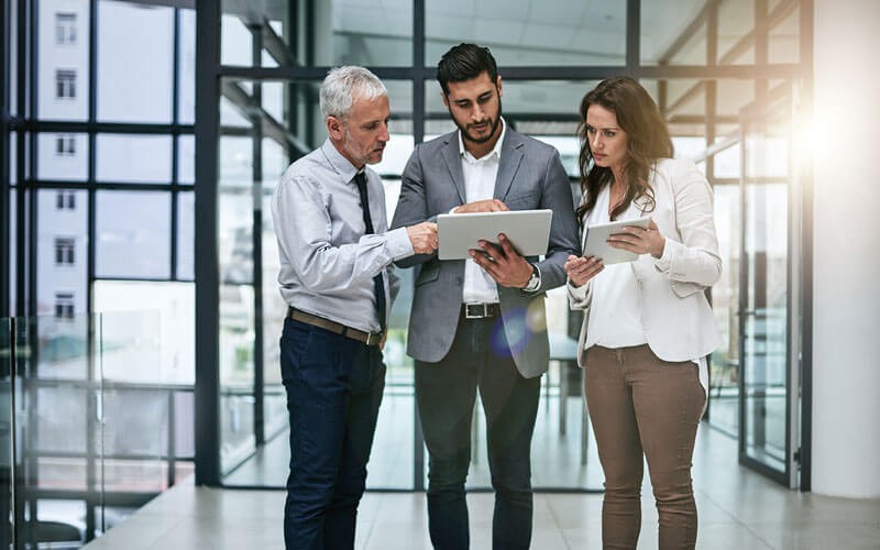 Three business professionals in hallway gathered around laptop computer