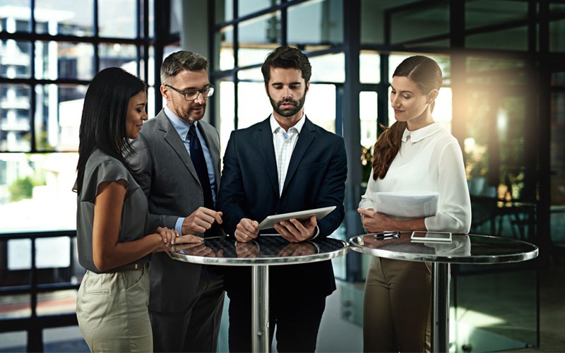 Four business employees standing at table looking at tablet
