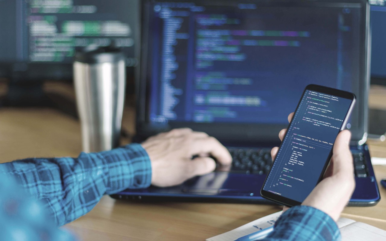 Man working on laptop holding a phone