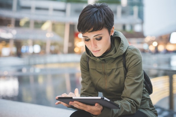 Woman in coat sitting outside looking at tablet