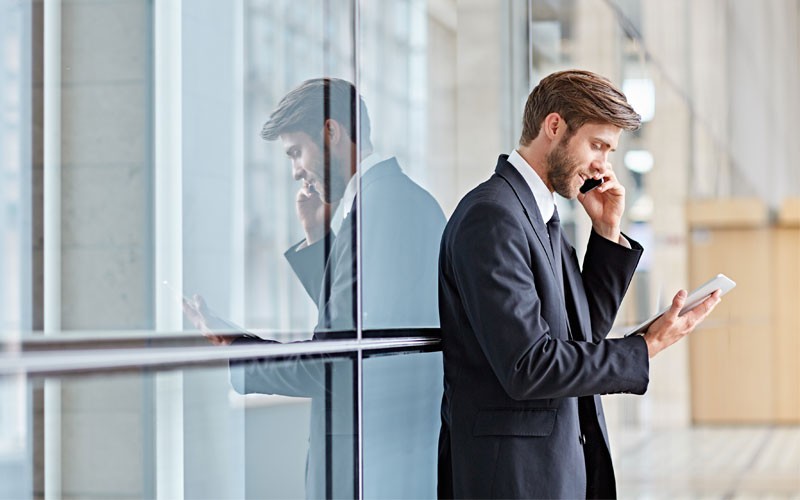 Business man outside building using mobile phone and tablet
