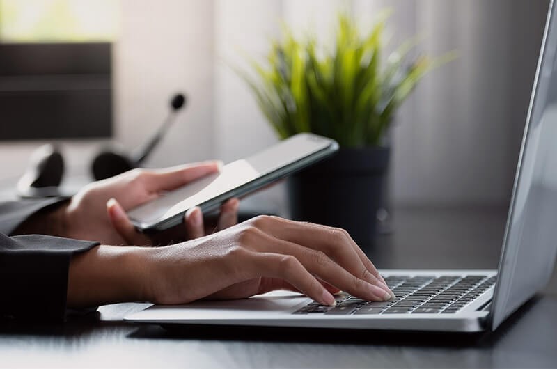 We do more than provide cloud products and tools Close up of hand holding a smart phone while typing on laptop