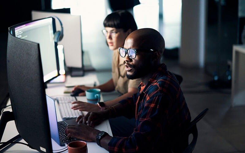 Two developers work on desktop computers in office at night