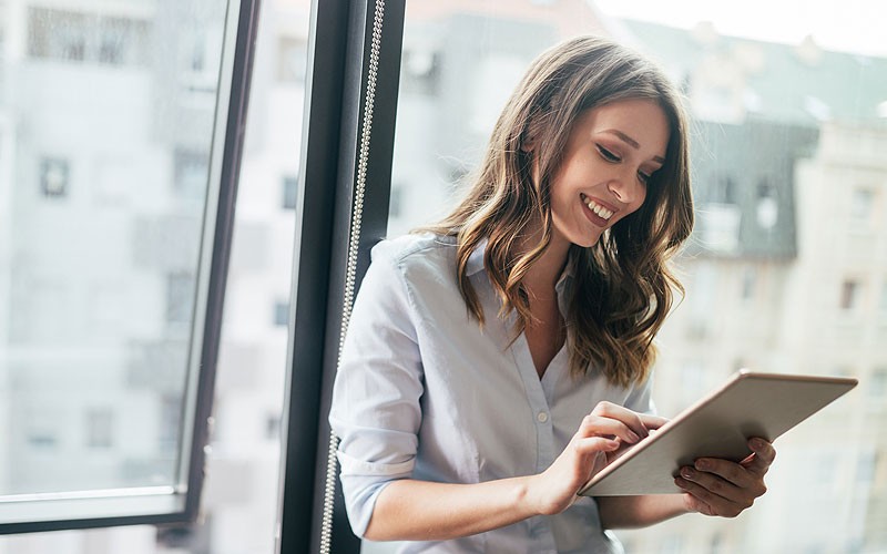 smiling-businesswoman-holding-tablet-in-front-of-window